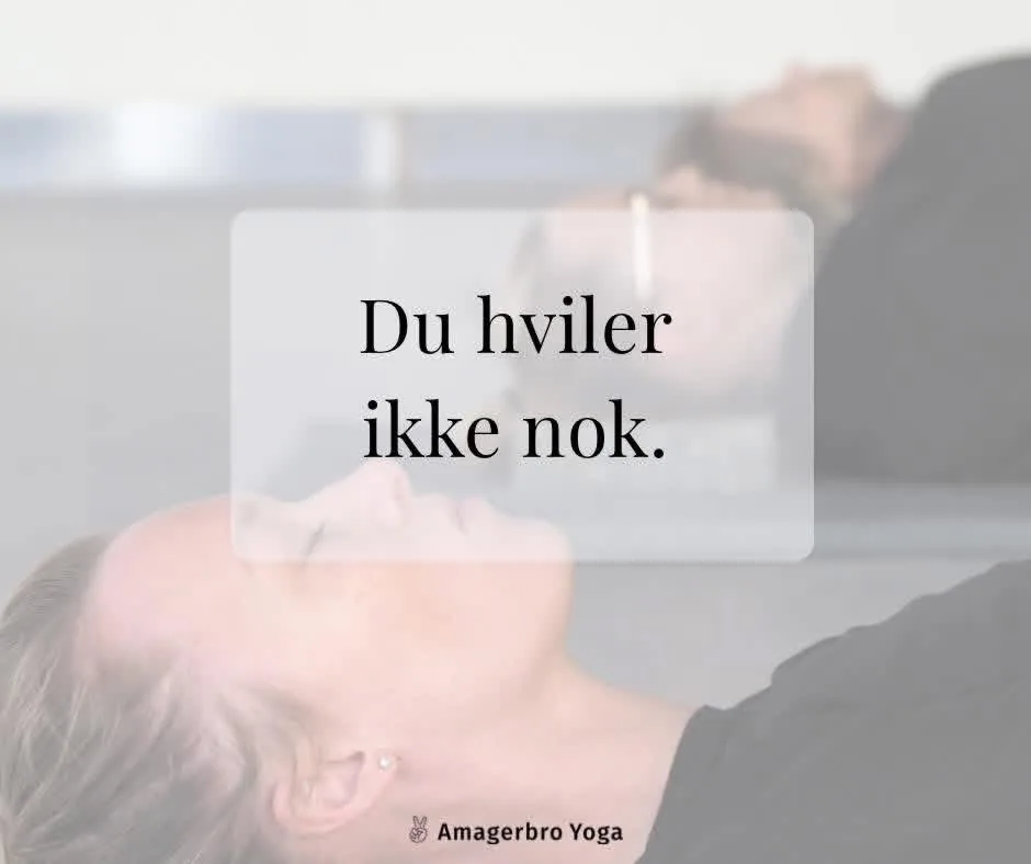 Kvinde ligger med lukkede øjne i afspænding efter en yogatime, med andre elever liggende i baggrunden