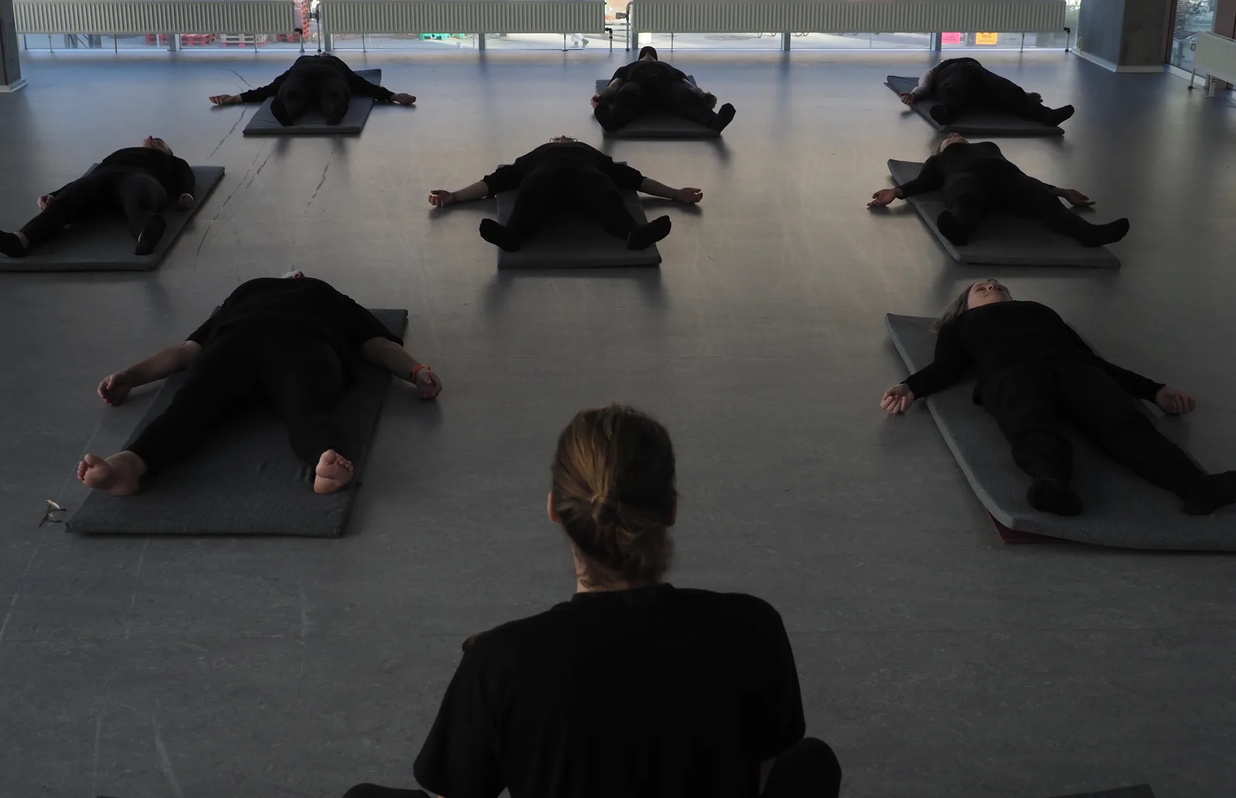 Holdet ligger i savasana på deres måtter i det dæmpede lys, mens underviseren sidder i forgrunden