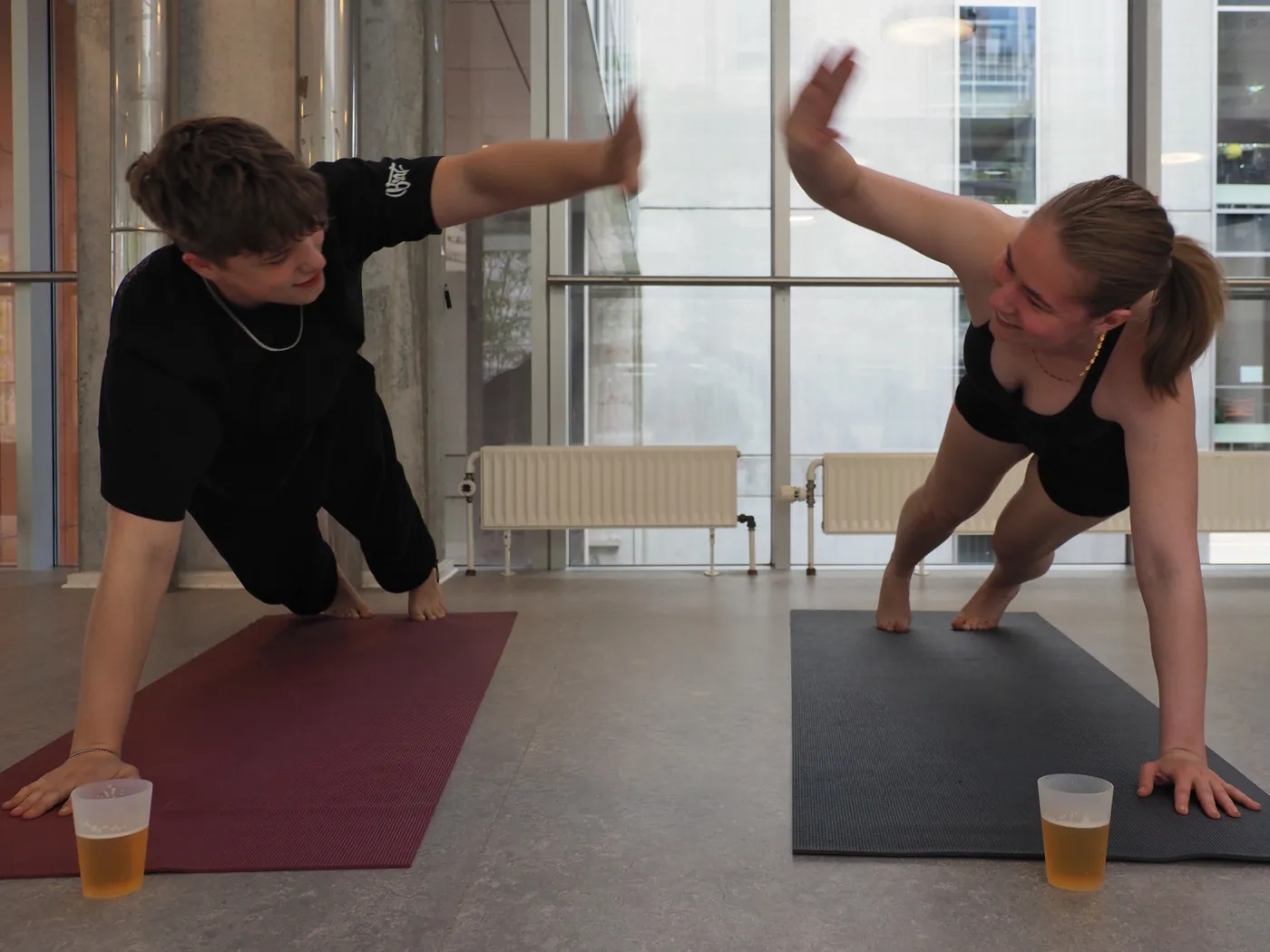 To deltagere giver high five i sideplanke med ølkrus på måtten